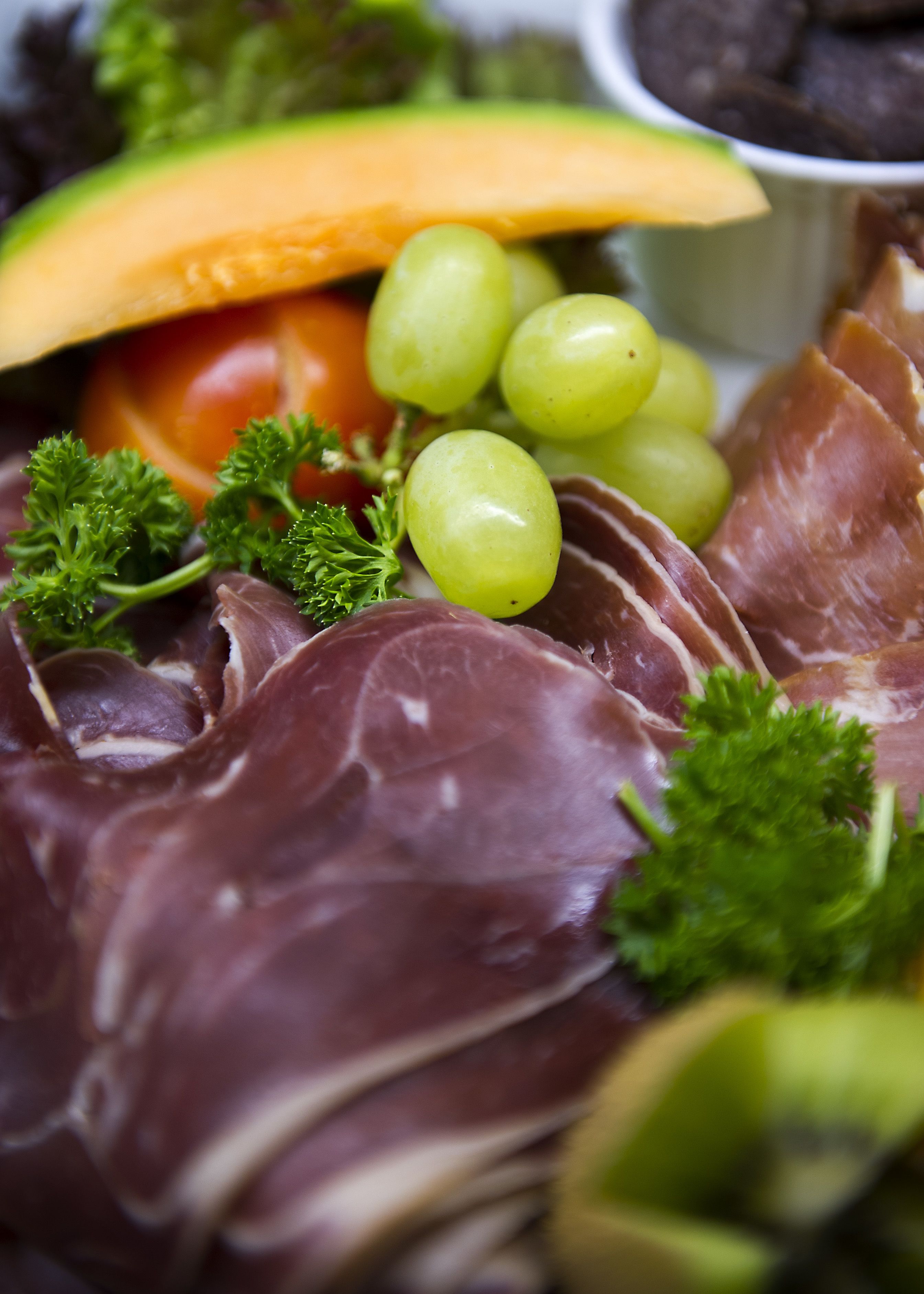 A platter of food including prosciutto, grapes, and a slice of melon.