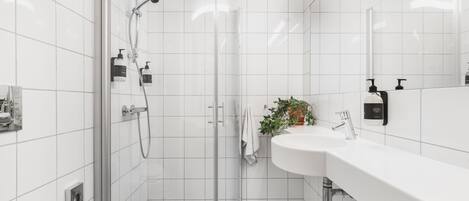A modern bathroom with a glass shower enclosure, a white sink, and a potted plant.