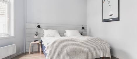 A modern bedroom with a bed, bedside tables, a framed picture, and a window.