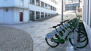 Una fila de bicicletas OBOS, verdes y blancas, estacionadas a lo largo de una acera junto a un edificio blanco con ventanas amplias.