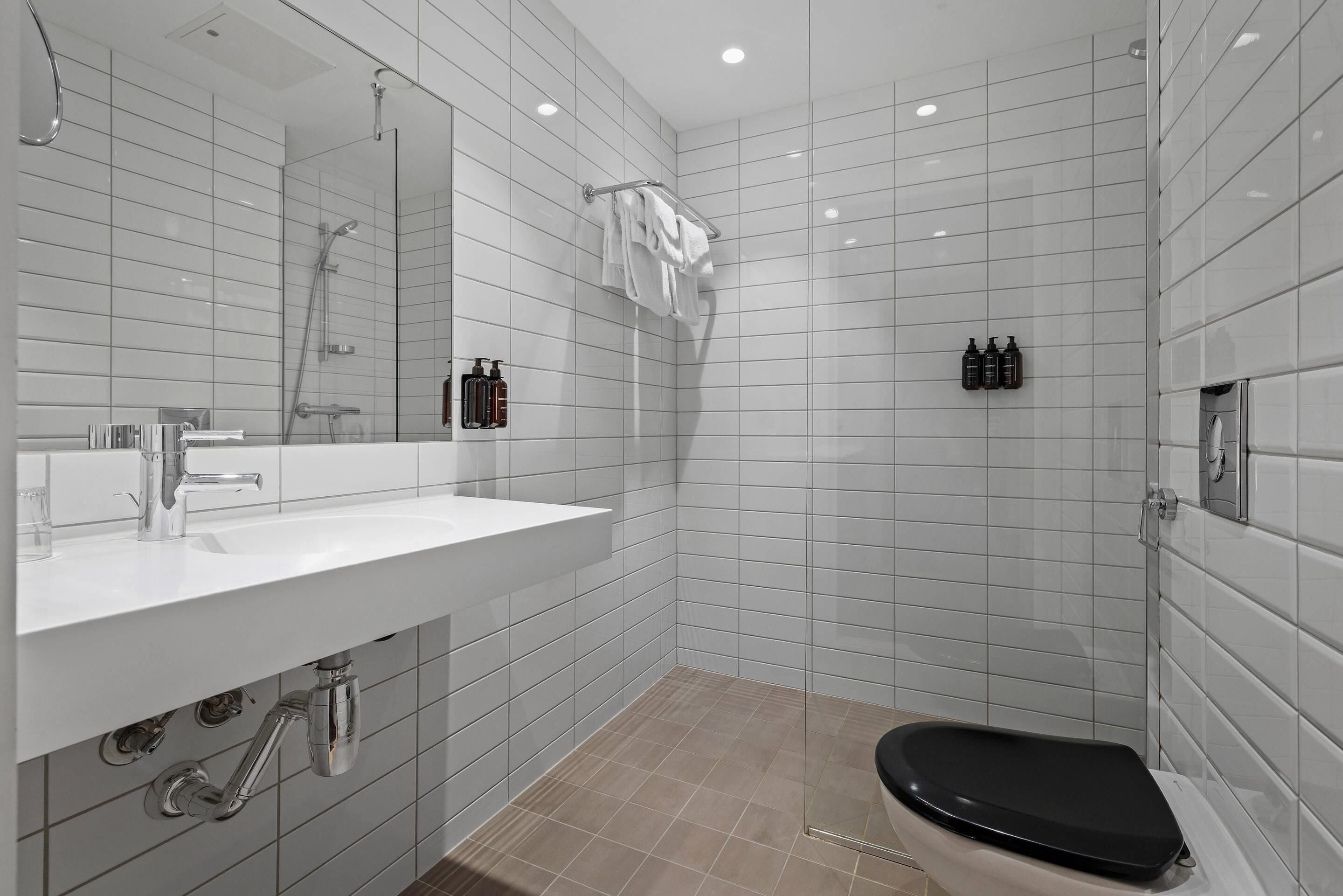 Une salle de bain moderne avec un lavabo blanc, un miroir et une douche. On y trouve des articles de toilette accrochés au mur et un porte-serviettes.