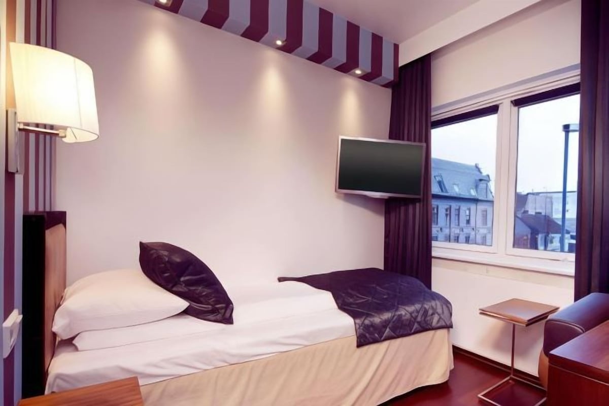 Habitación de hotel con cama, televisión, una mesita y ventana con vistas a edificios.