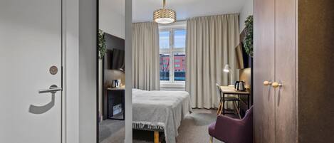 Habitación de hotel con cama, escritorio, silla, televisor y ventana con cortinas.
