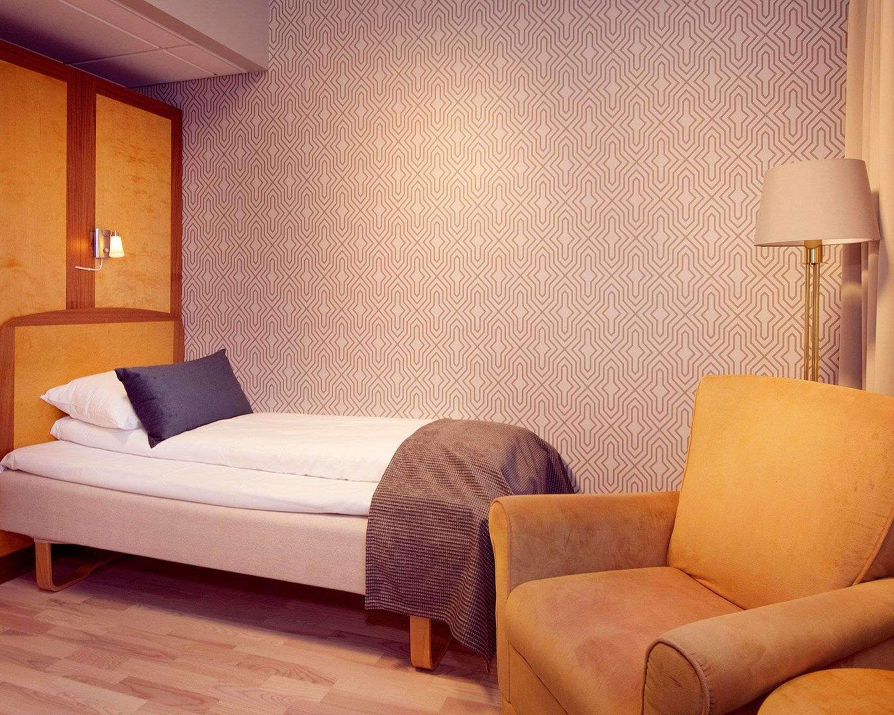 Un dormitorio ordenado con una cama, una silla y una lámpara.