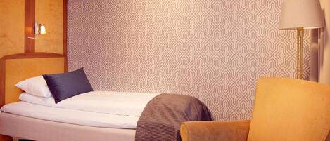 A neatly arranged bedroom with a bed, a chair, and a lamp.