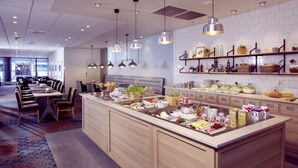 Een modern restaurantgedeelte in een hotel, met een centraal eiland, diverse zitplaatsen en verschillende stations voor eten en drinken.