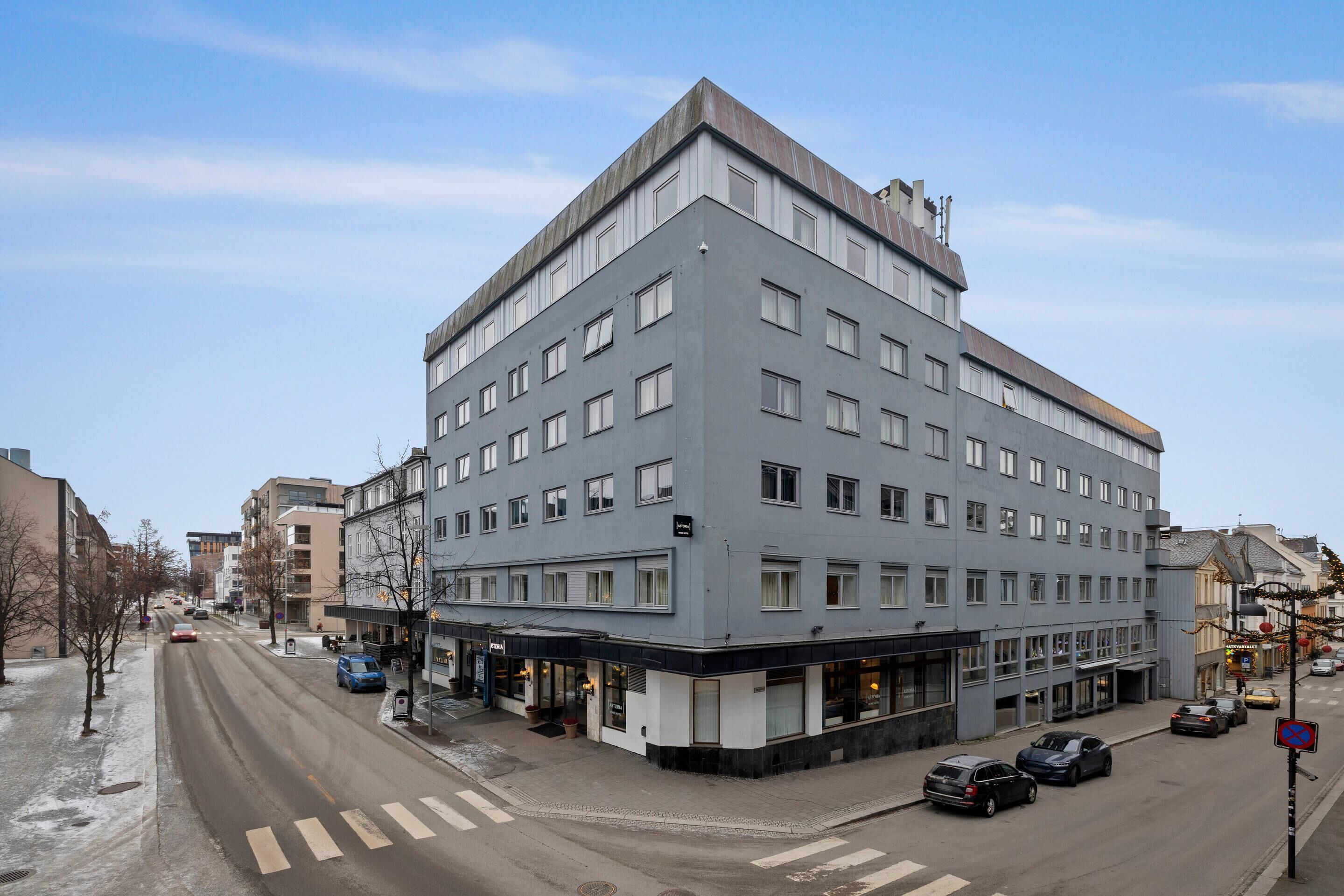 Un hotel de varios pisos con diseño moderno, ubicado en una esquina con entrada visible y área de estacionamiento.