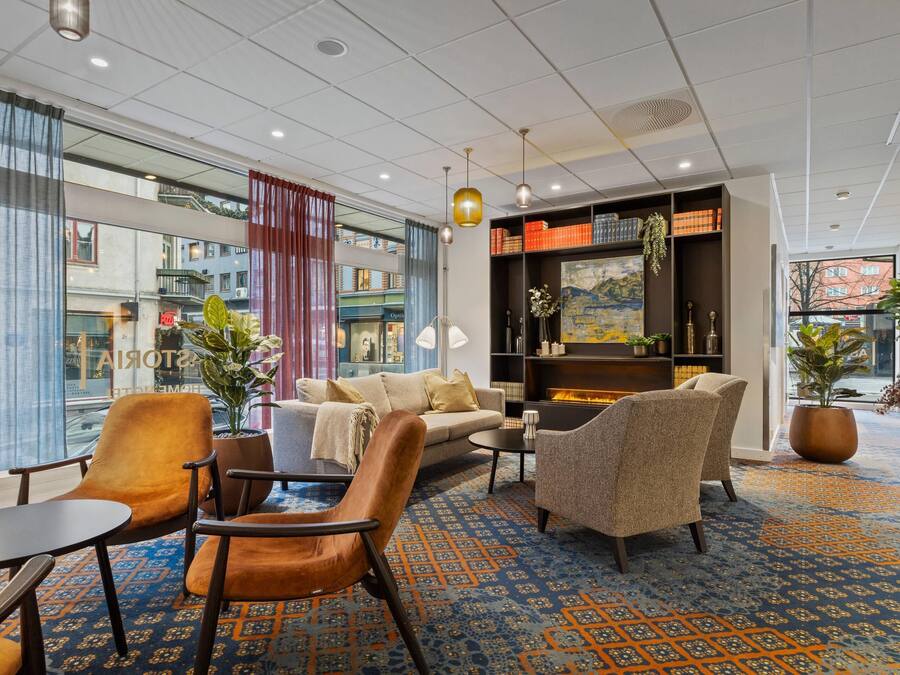 A modern hotel lobby with a seating area, large windows, and a fireplace.