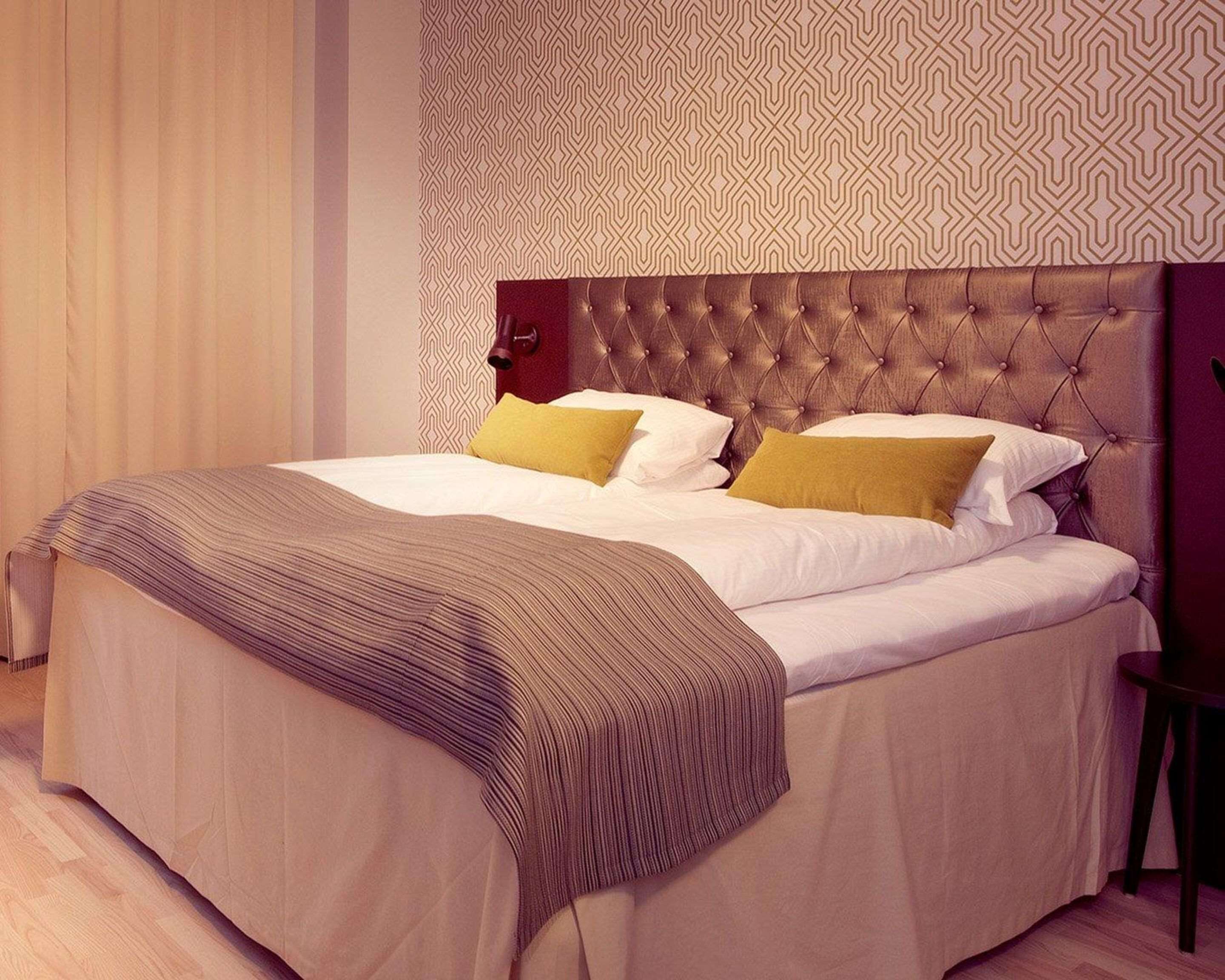 A neatly made bed with a striped throw, a tufted headboard, and patterned wall decor.