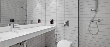 Un baño moderno con pared de azulejos blancos, un espejo grande, un lavabo blanco, un inodoro y una zona de ducha.