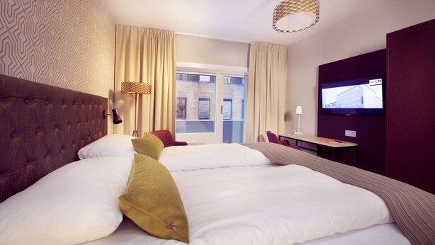 Een hotelkamer met een groot bed, een bureau, een televisie en een raam met uitzicht op gebouwen.