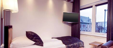 Habitación de hotel con cama, televisión montada en la pared, una mesita y ventana con vistas a edificios.