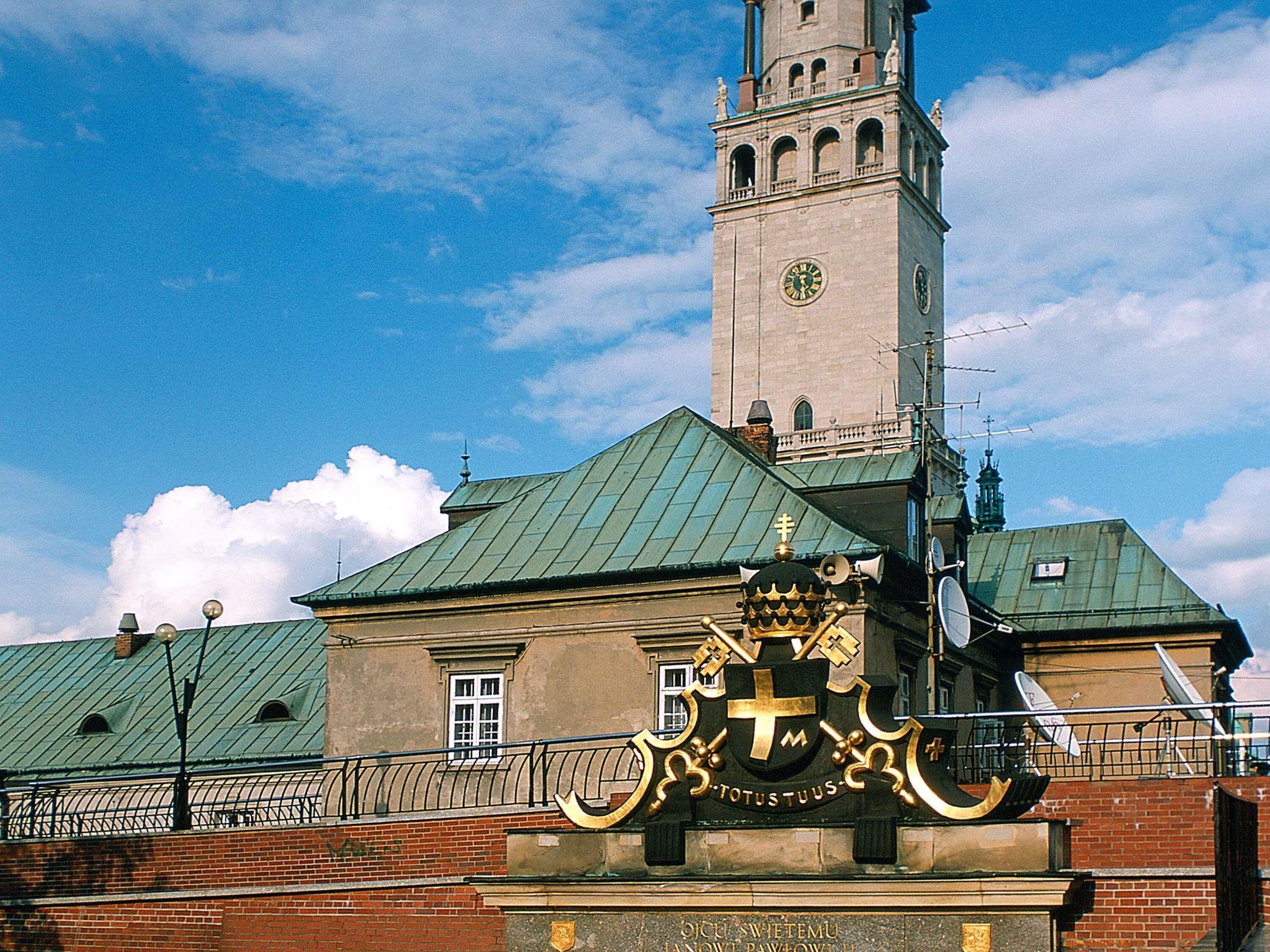 Historiallinen rakennus, jossa on kellotorni, huomiota herättävä vaakuna ja vihreä katto.
