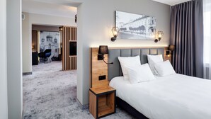 Una habitación de hotel moderna con una cama grande, cabecera con iluminación integrada, una mesita de noche y un televisor montado en la pared.