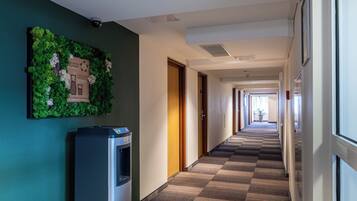 A hotel hallway with a checkered carpet, a water dispenser, and a wall-mounted plant.