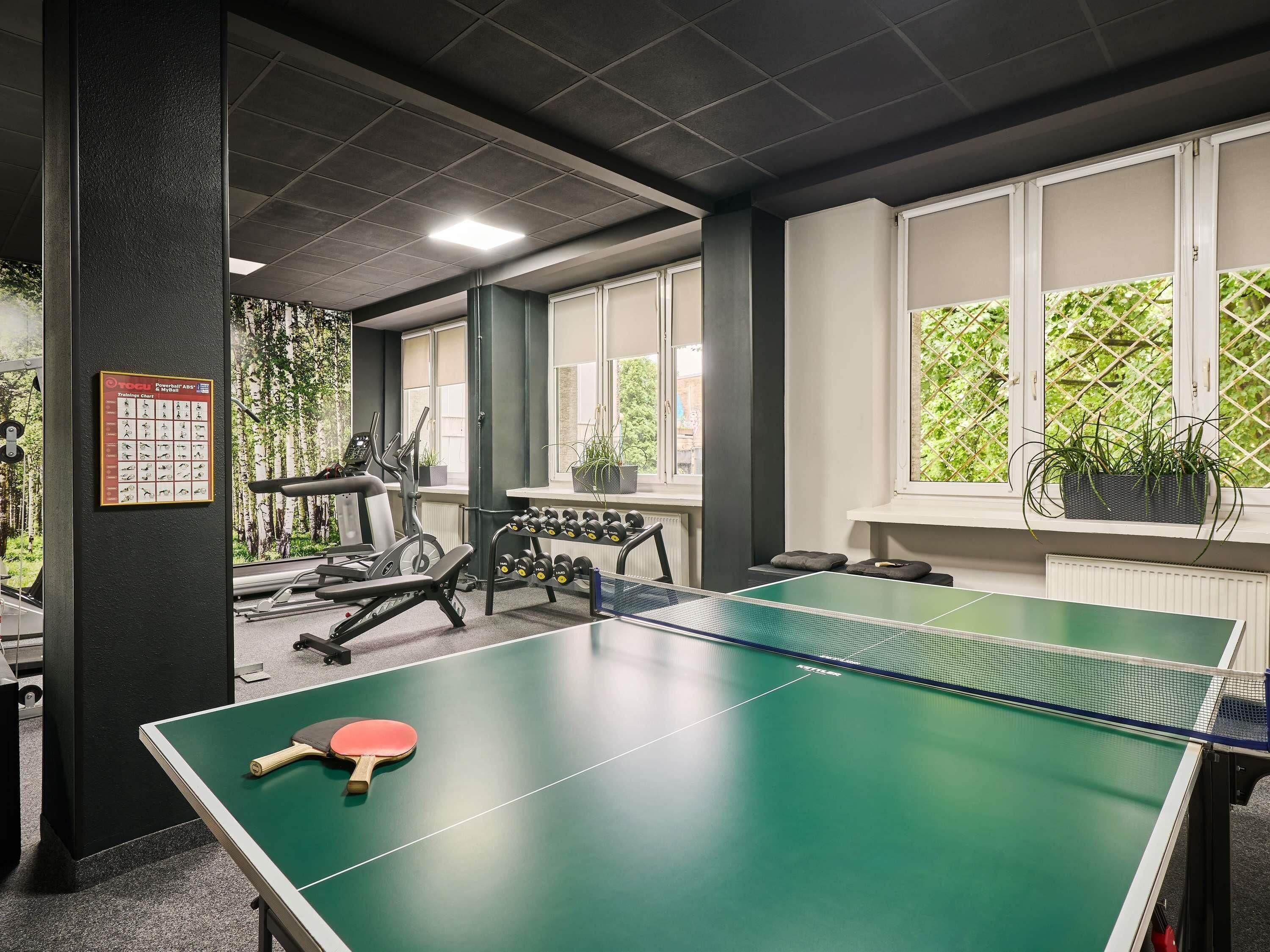 Una mesa de ping pong con una paleta, equipo de ejercicio y un gráfico de acondicionamiento físico en la pared.