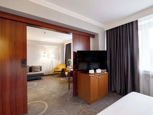 Habitación de hotel con una cama grande, un armario de madera, un televisor de pantalla plana, un escritorio con lámpara, un sofá y una silla.