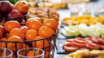 Una mesa de buffet con diversos alimentos, incluyendo naranjas, frutas y pasteles.