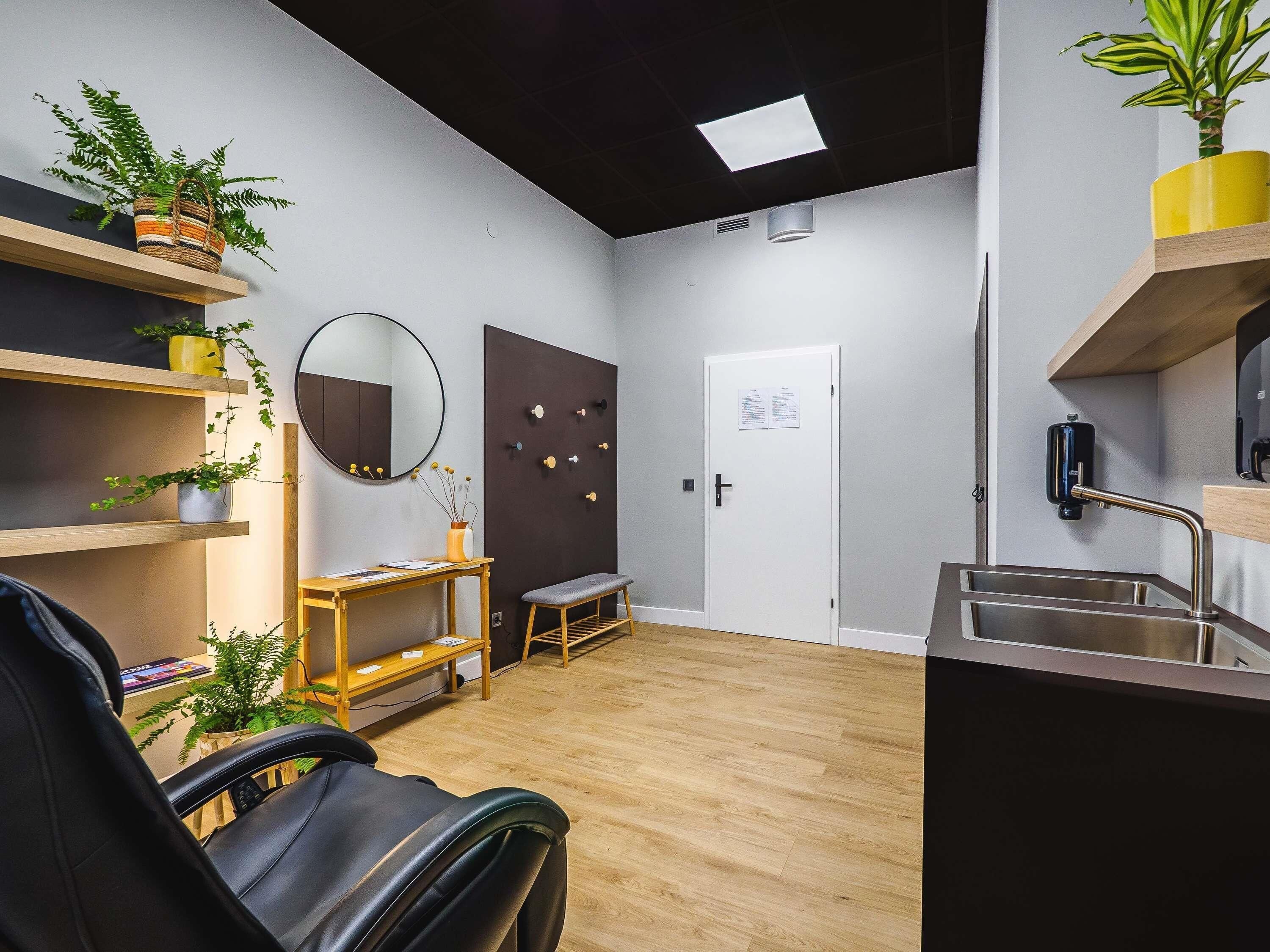 A modern room with a wheelchair, wooden flooring, a desk, a bench, a mirror, a door, and a sink.