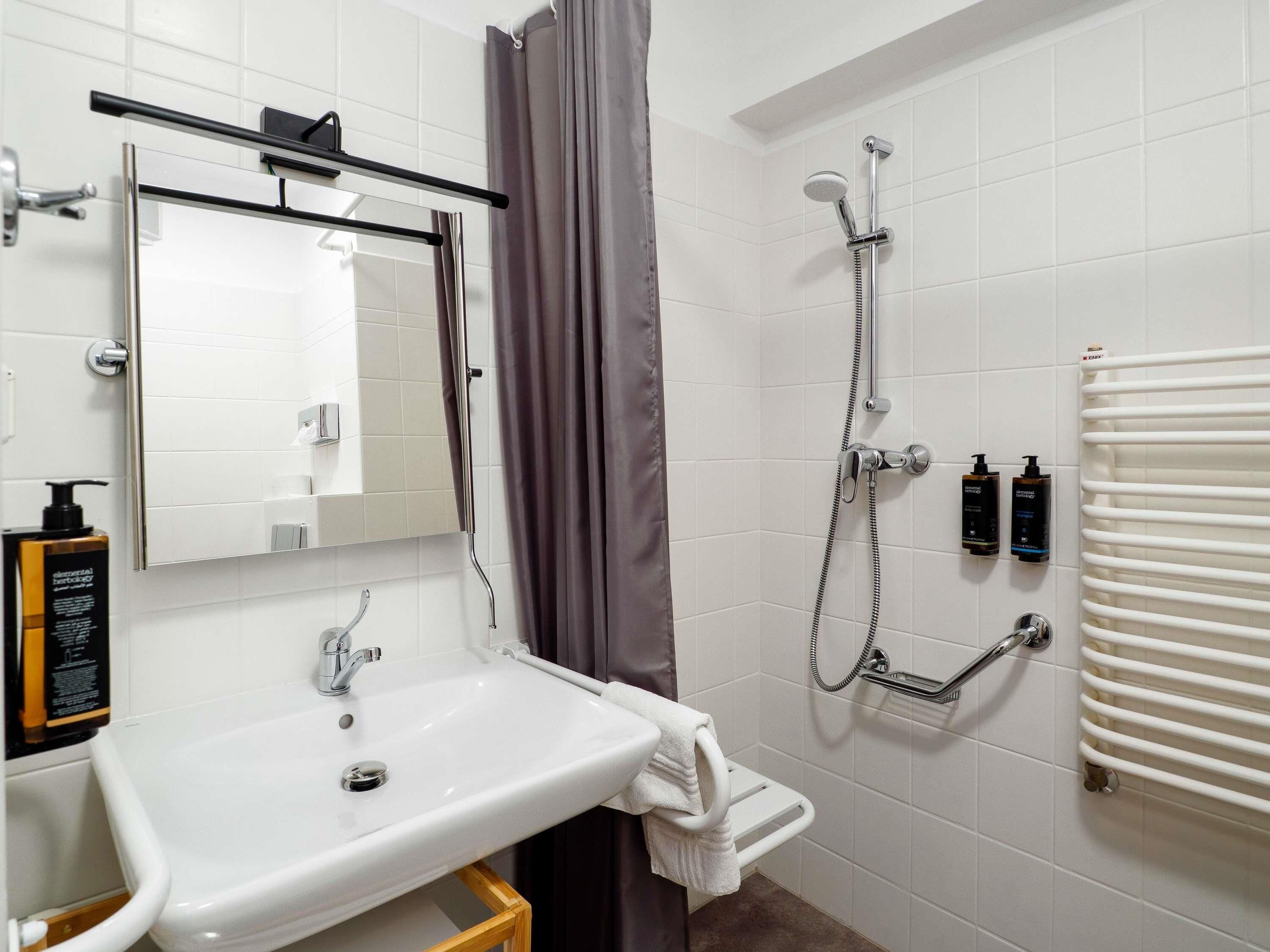 A modern bathroom with a white sink, a mirror, a shower with a handheld showerhead, and a towel rack.