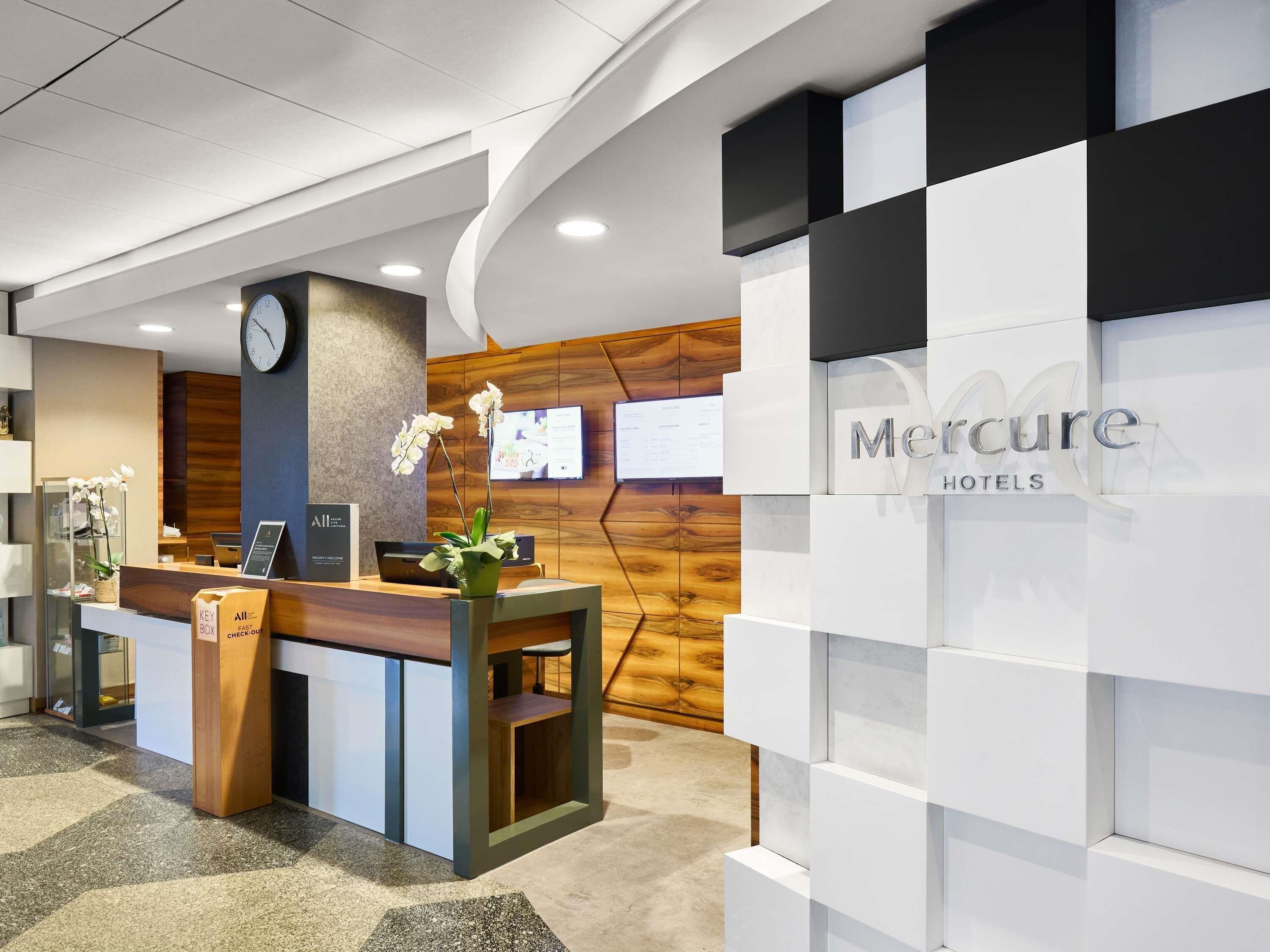 A reception desk with a clock, a digital screen, and a sign for Mercure Hotels.