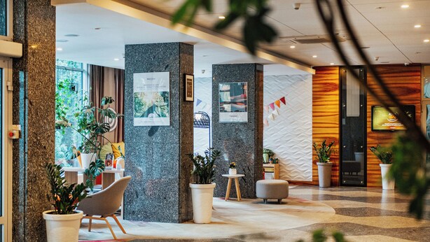 Un vestíbulo moderno con una recepción de mármol, asientos cómodos, plantas en macetas y vistas al exterior.