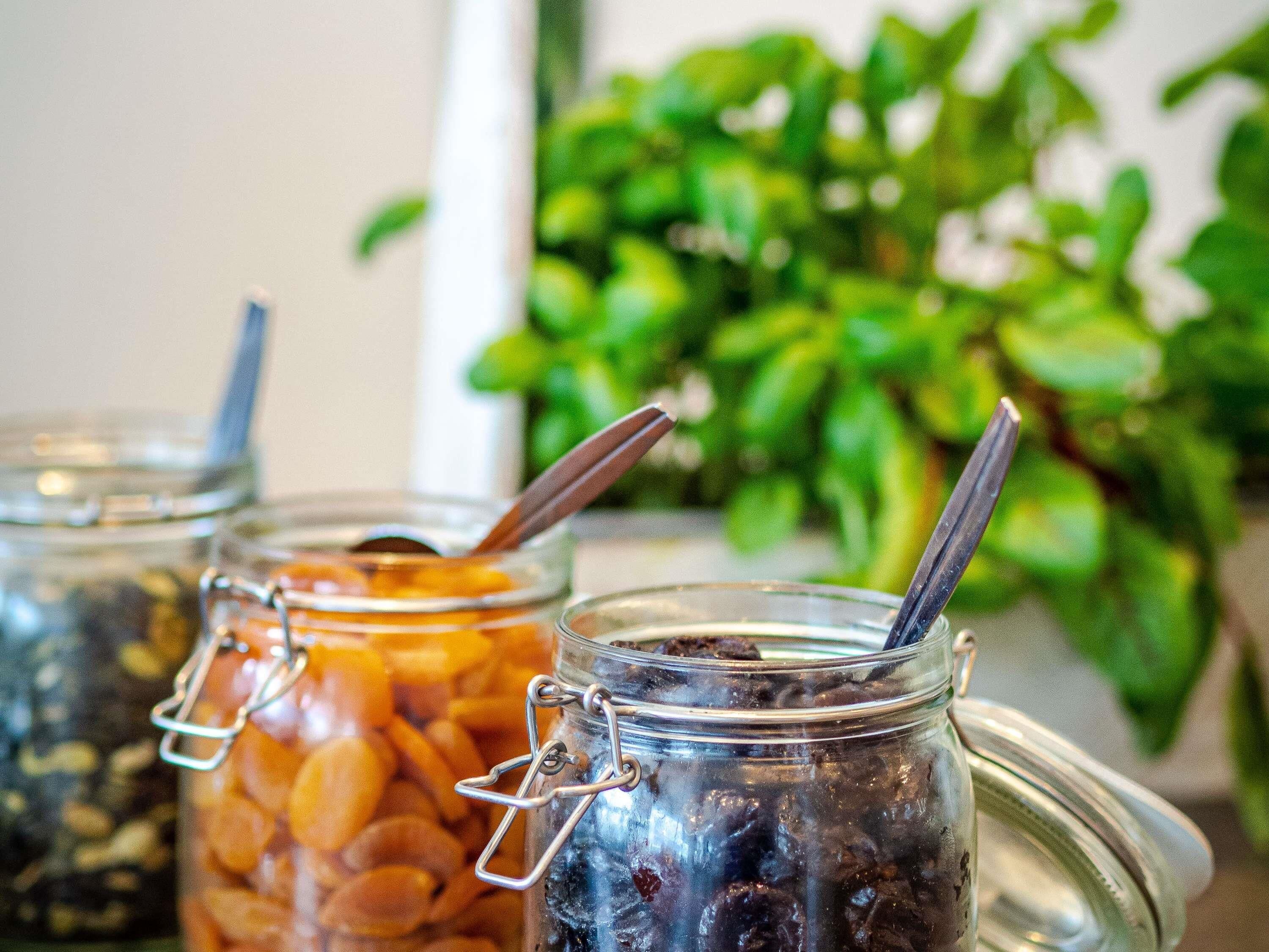 Three glass jars with metal clasps containing dried fruits and a spoon in each.