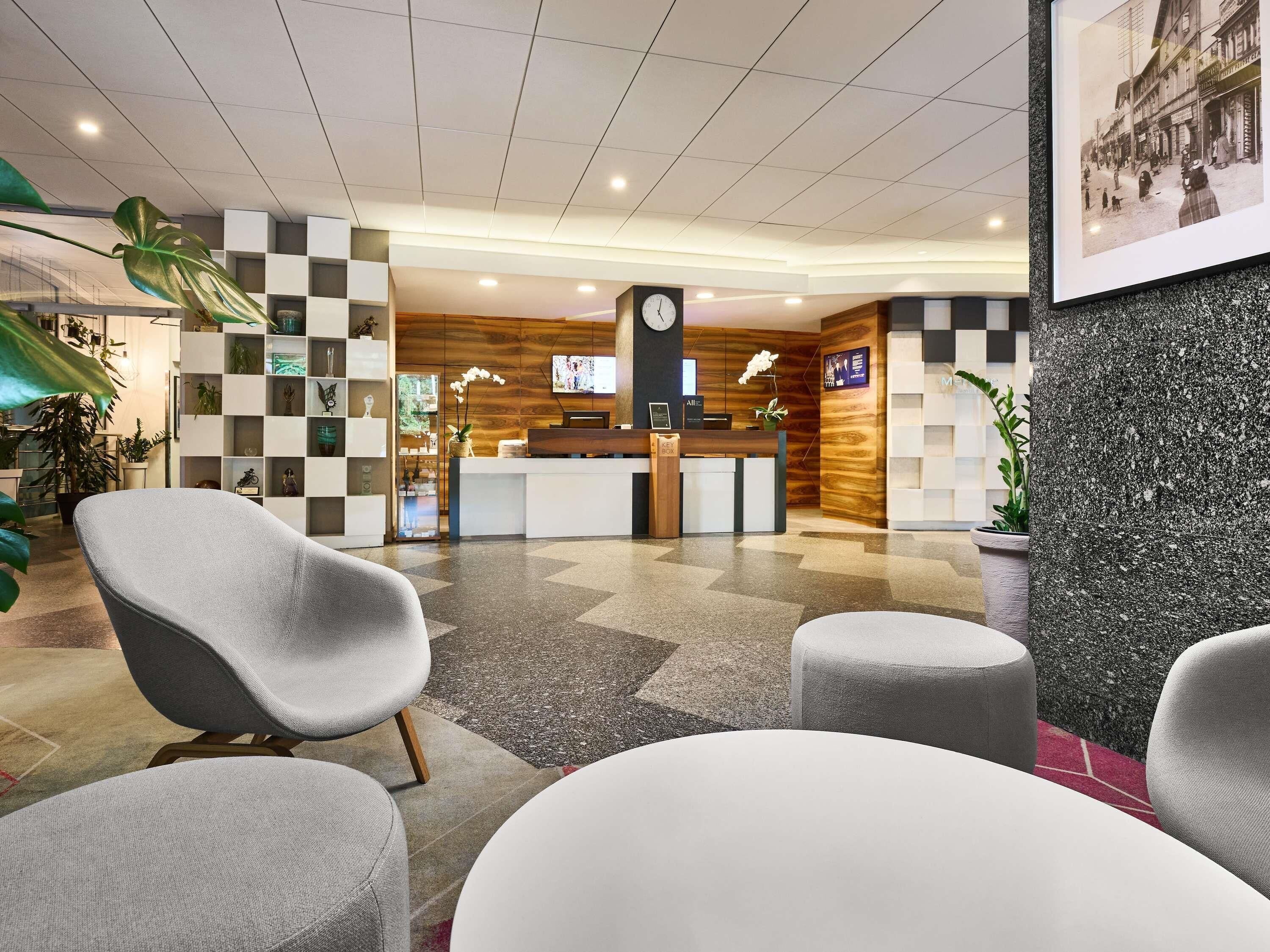 Un espace d’accueil comprenant un comptoir d’enregistrement, un coin salon avec des chaises, une horloge et un téléviseur.
