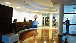 Un vestíbulo de hotel con una recepción, un área de descanso y la entrada a un restaurante.