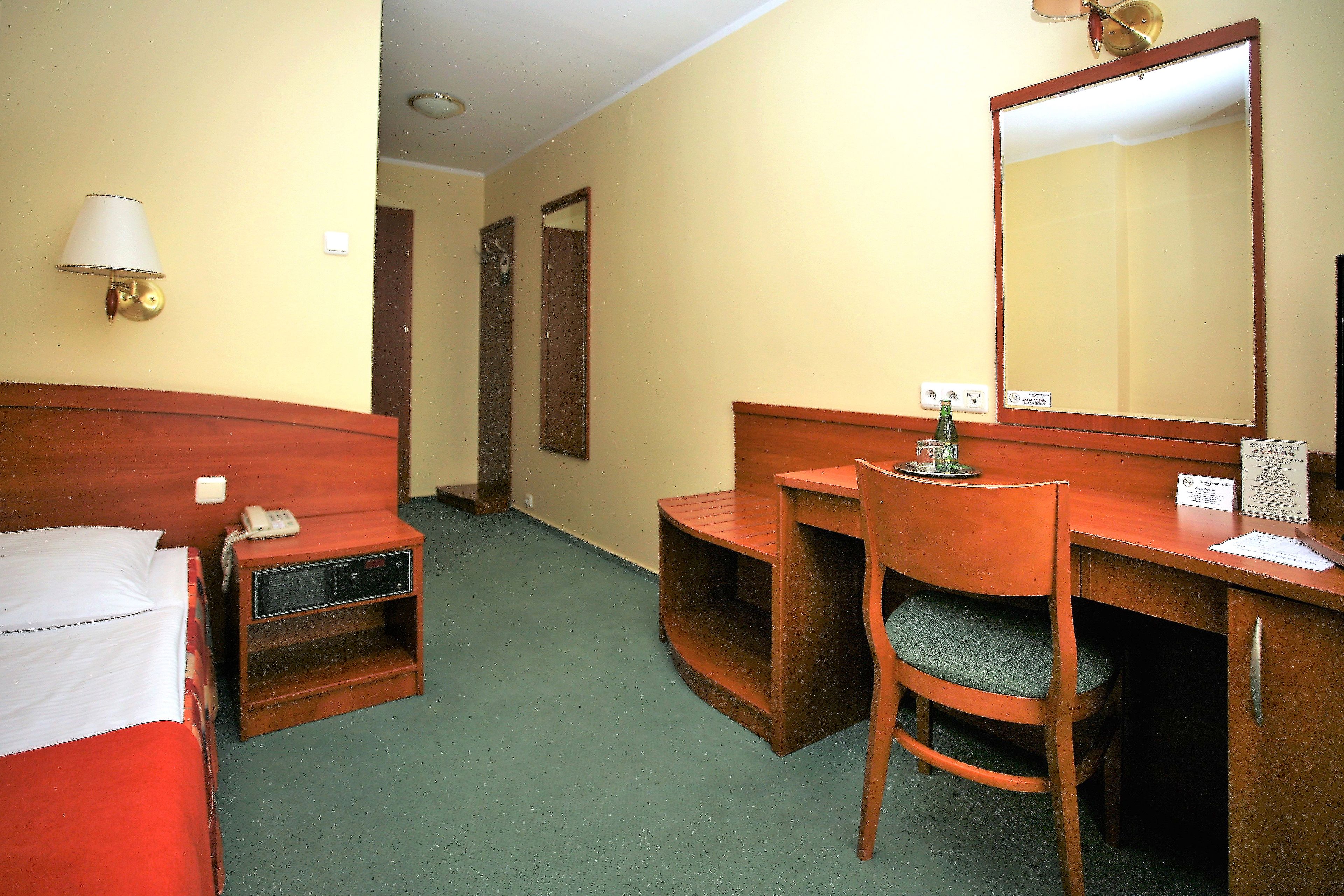 A hotel room with a bed, a desk with a chair, a telephone, a lamp, and a mirror.