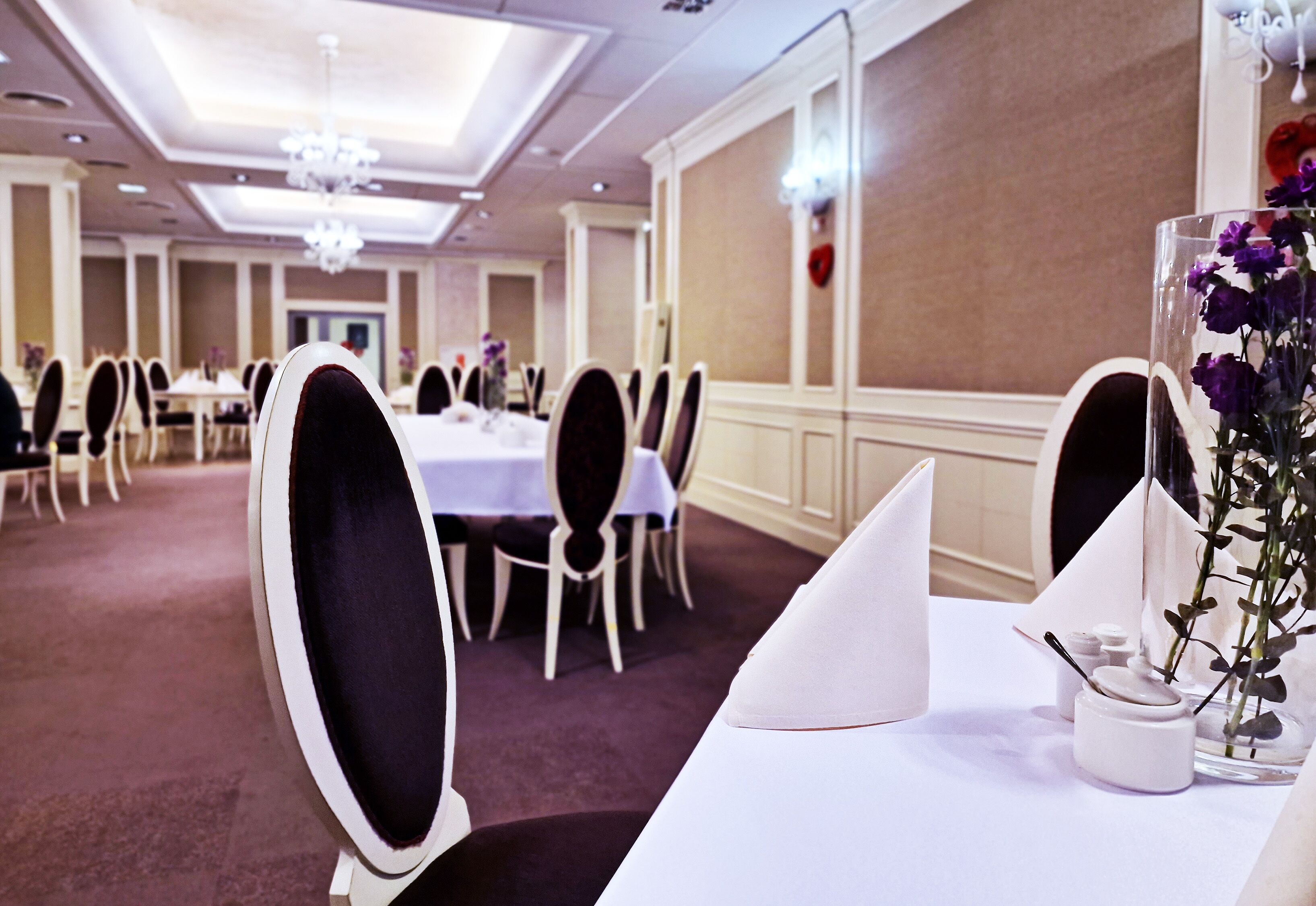 A banquet hall with round tables, white tablecloths, and black chair cushions.