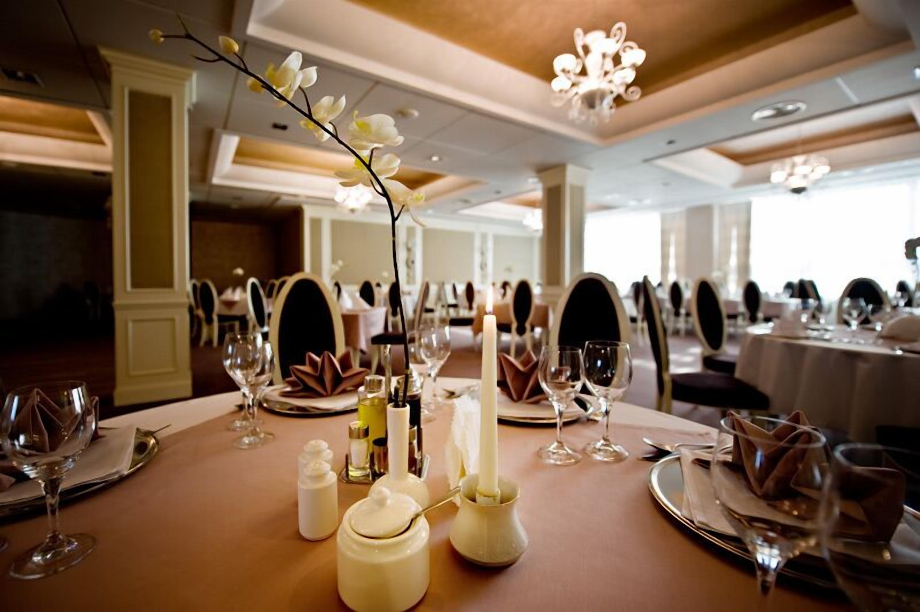 Un salón de banquetes con mesas redondas dispuestas para cenar, cada una con mantel blanco, velas y cristalería.