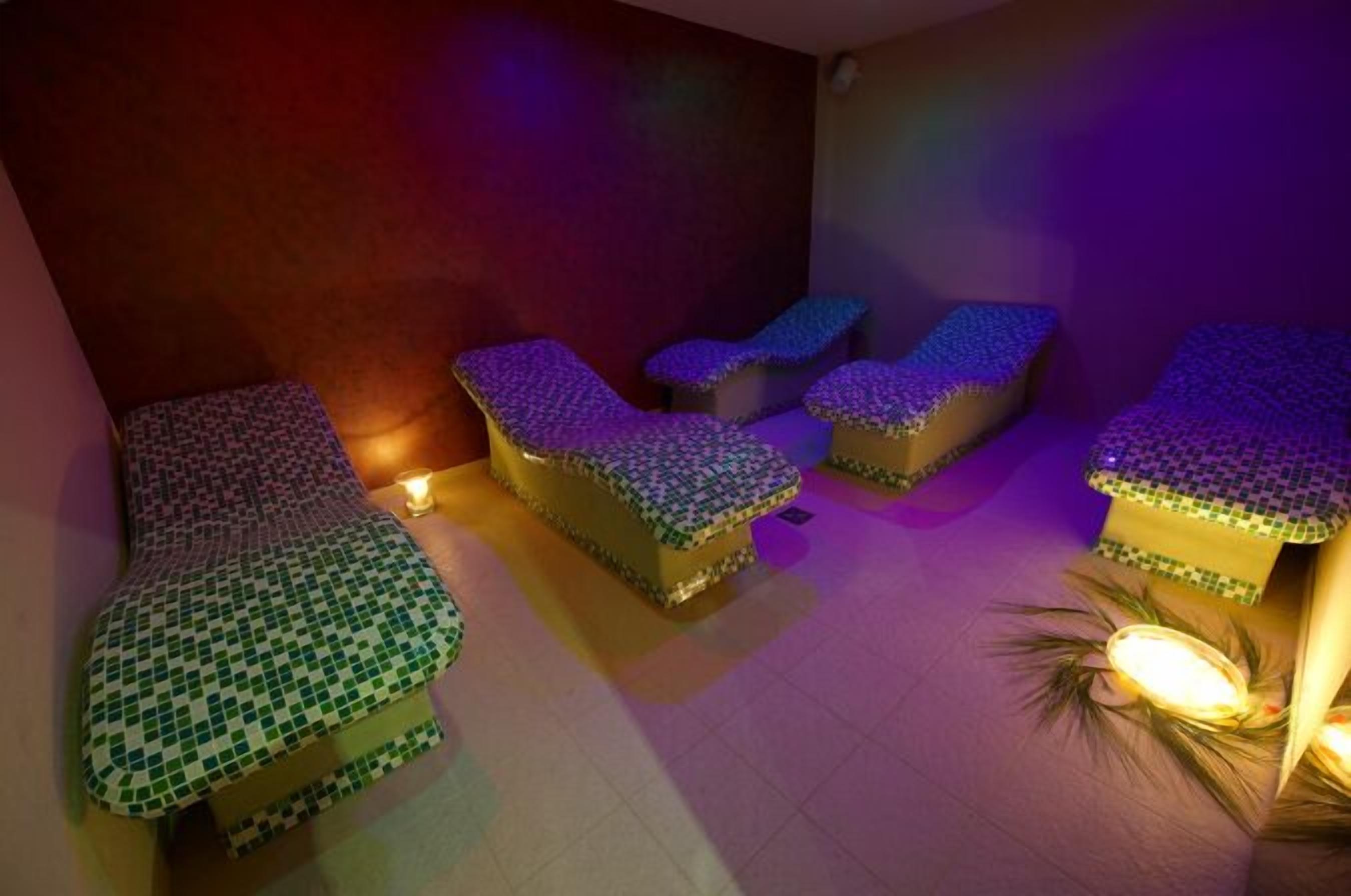 A room with four massage tables covered in patterned mats, a small table with a candle, and a plant.