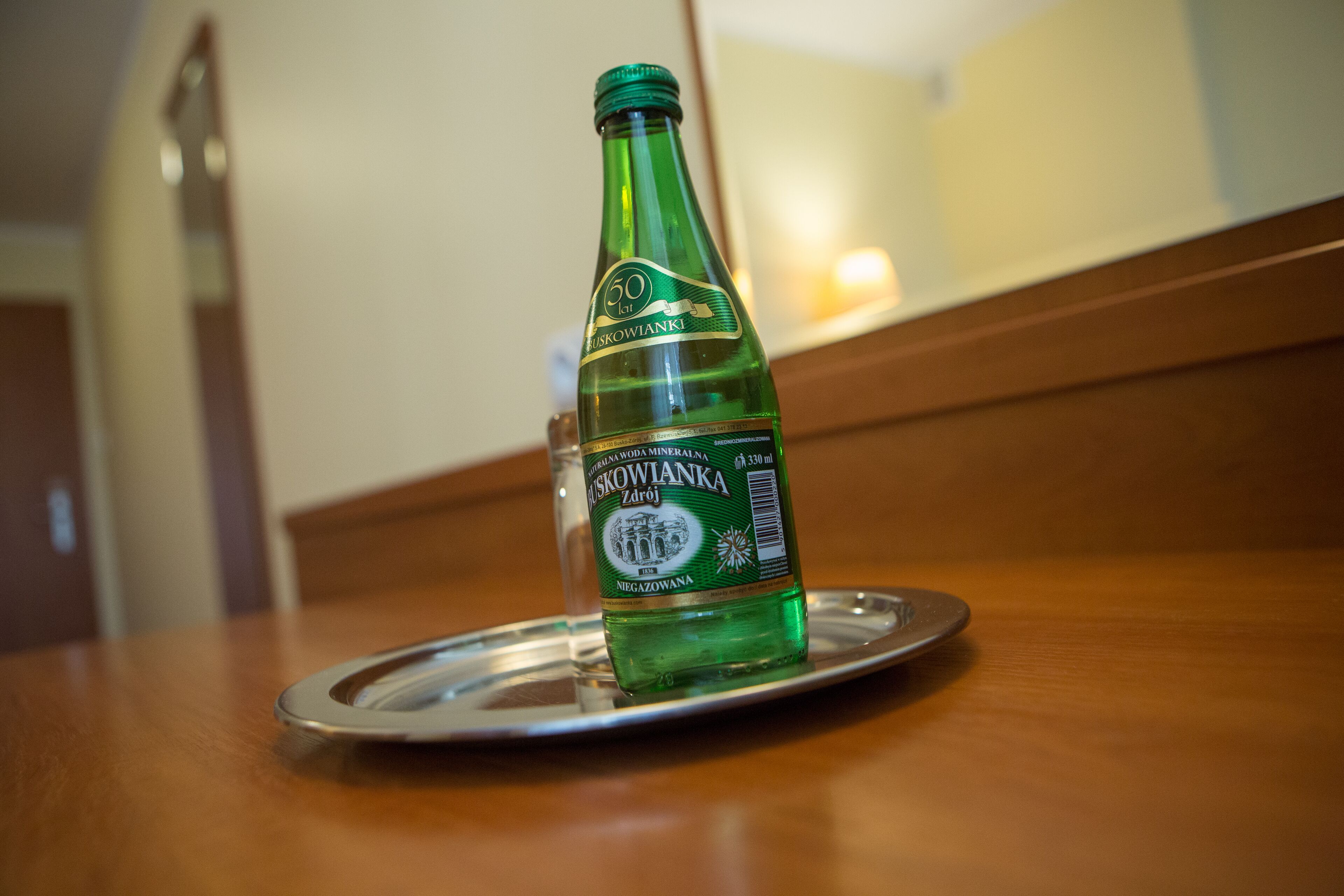 A green bottle of Zdziorajka mineral water on a metal tray on a wooden table.