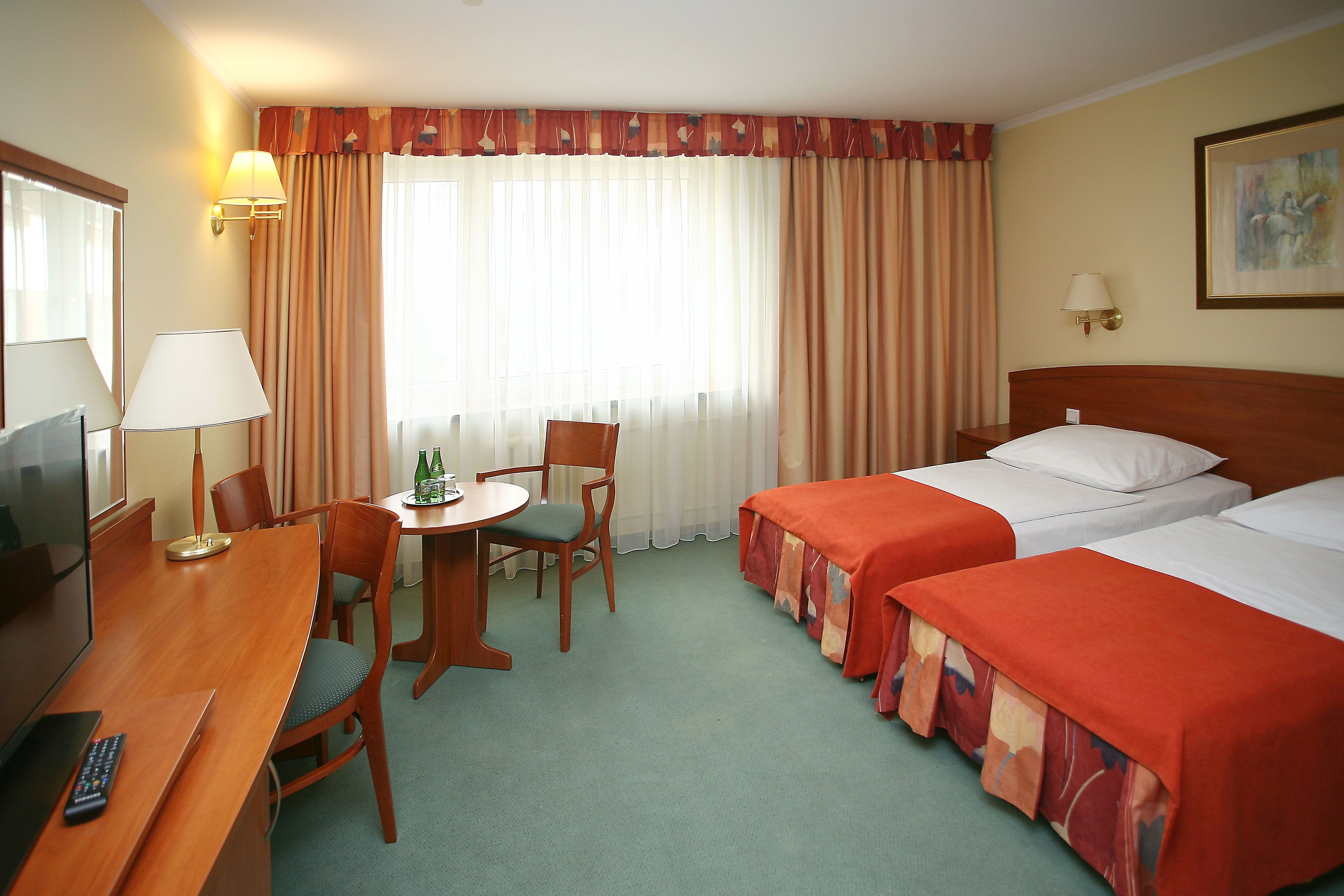Habitación de hotel con dos camas, un escritorio con silla, televisor y ventana con cortinas.