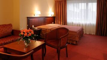 Una habitación de hotel con cama, escritorio con silla, sofá y un jarrón de flores.
