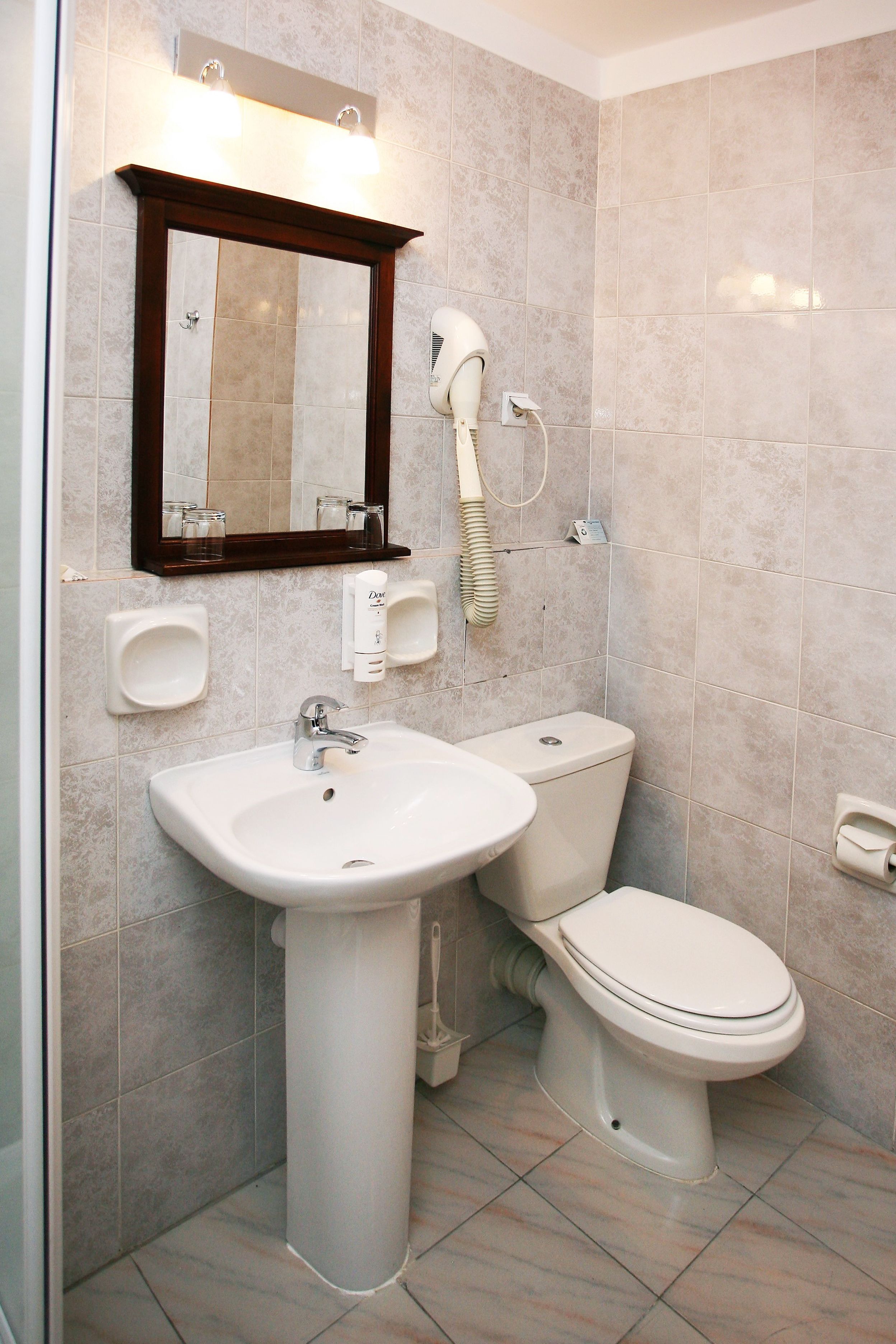 A bathroom with a pedestal sink, a toilet, a hairdryer, and a mirror.