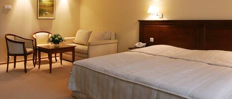 Habitación de hotel con una cama grande, una silla, una mesita con un florero y una lámpara en la pared.