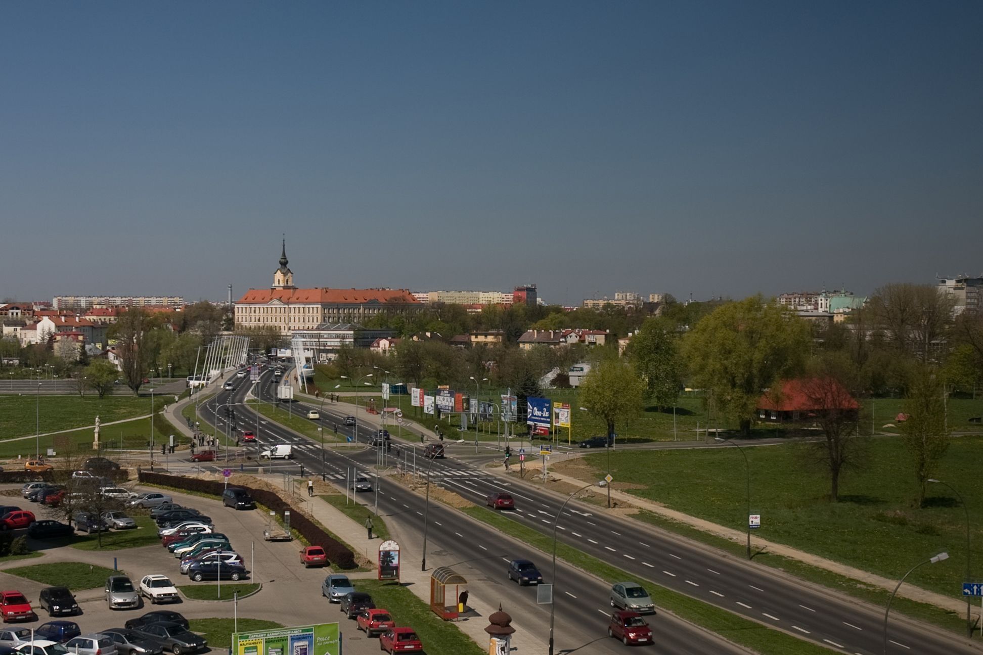 A cityscape with a prominent building with a tower, multiple roads, and a parking area.
