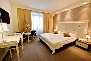 Habitación de hotel con cama, mesita de noche, lámpara, escritorio, silla y una pequeña mesa con un jarrón de flores.