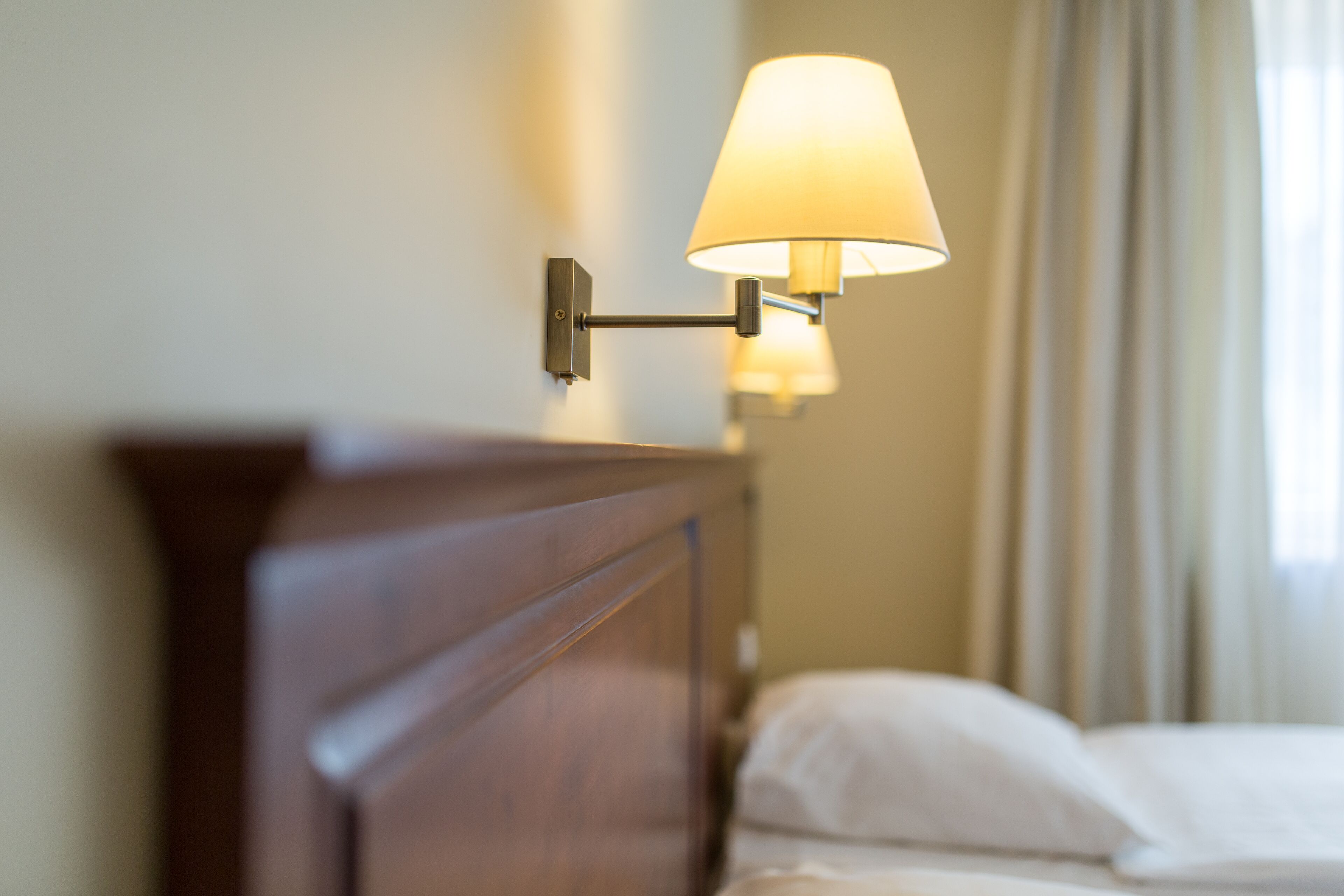 A wall-mounted lamp with a white shade, a wooden headboard, and a bed with white bedding.