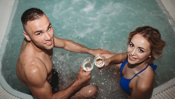 Dos personas en un jacuzzi, sosteniendo copas.