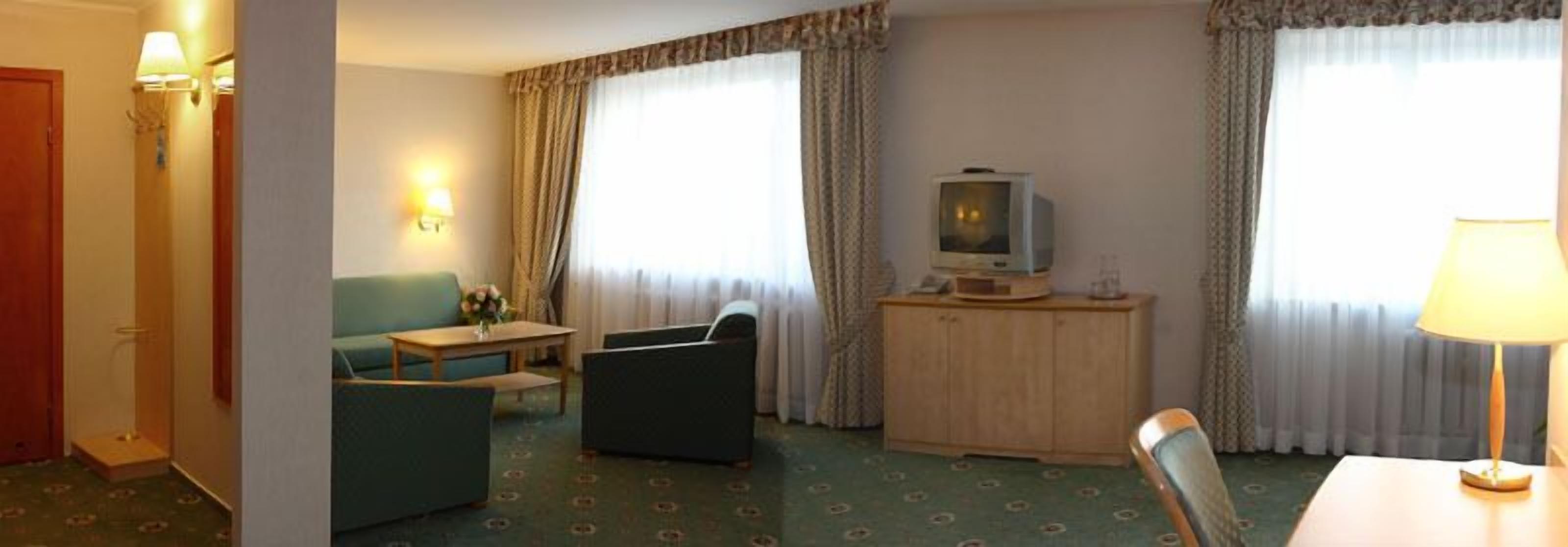 Una habitación de hotel con sofá, una mesita, un televisor en un mueble y una lámpara.
