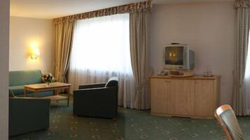A hotel room with a sofa, a small table, a television on a cabinet, and a lamp.