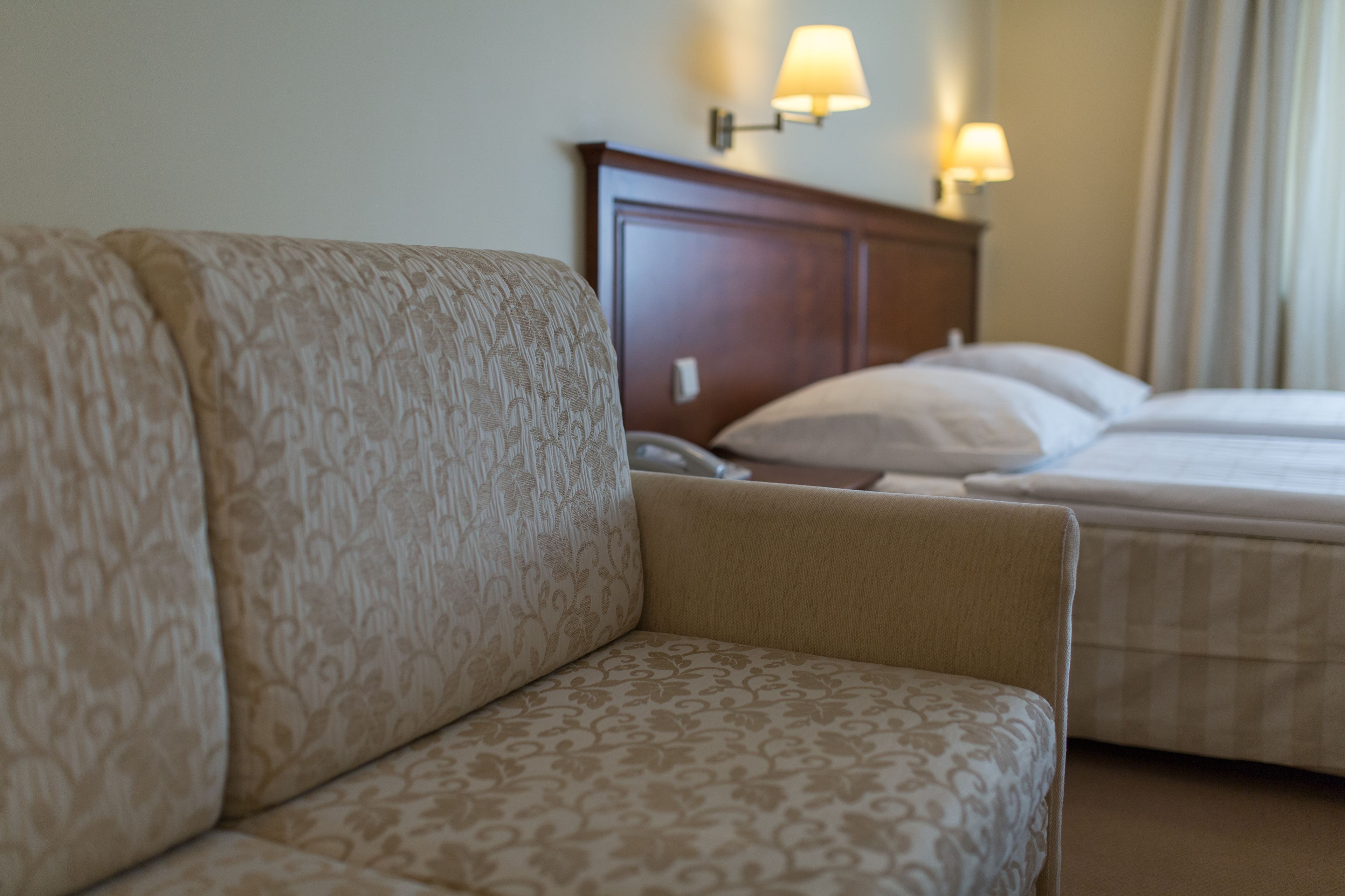 A hotel room with a patterned sofa, a wooden headboard, and two bedside lamps.