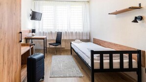 A compact hotel room with a single bed, a desk with a chair, a television mounted on the wall, and a suitcase on the floor. - Hotel Alf (Krakow)