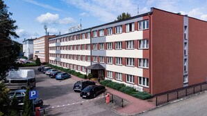 A hotel with a red and white facade, multiple windows, and a parking lot with several cars. - Hotel Alf (Krakow)