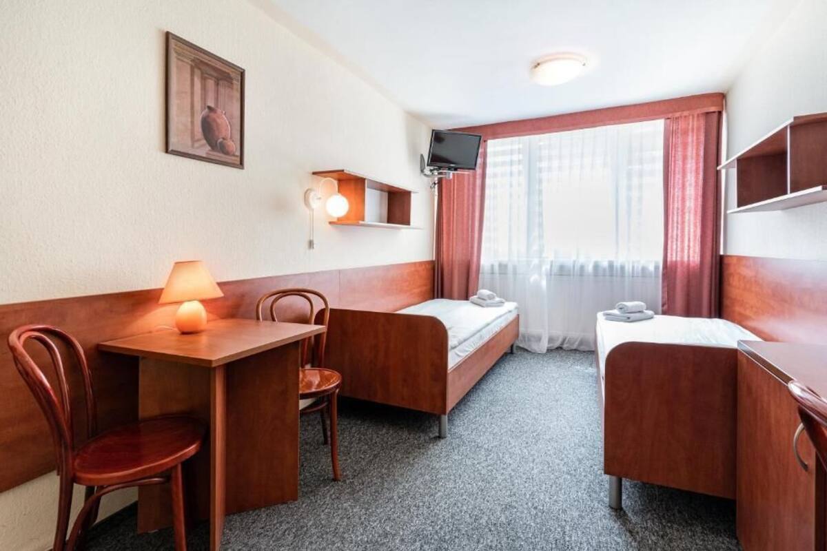 Une chambre d’hôtel de taille modeste, comprenant un lit, un bureau, une chaise, une télévision et une fenêtre avec des rideaux.