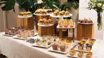 Una mesa de buffet con diversos alimentos y postres, incluyendo sándwiches, pasteles y copas de fruta.