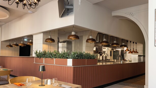 A modern restaurant with a wooden dining area, a central island with plants, and pendant lighting. - Hotel Cristal (Bialystok)